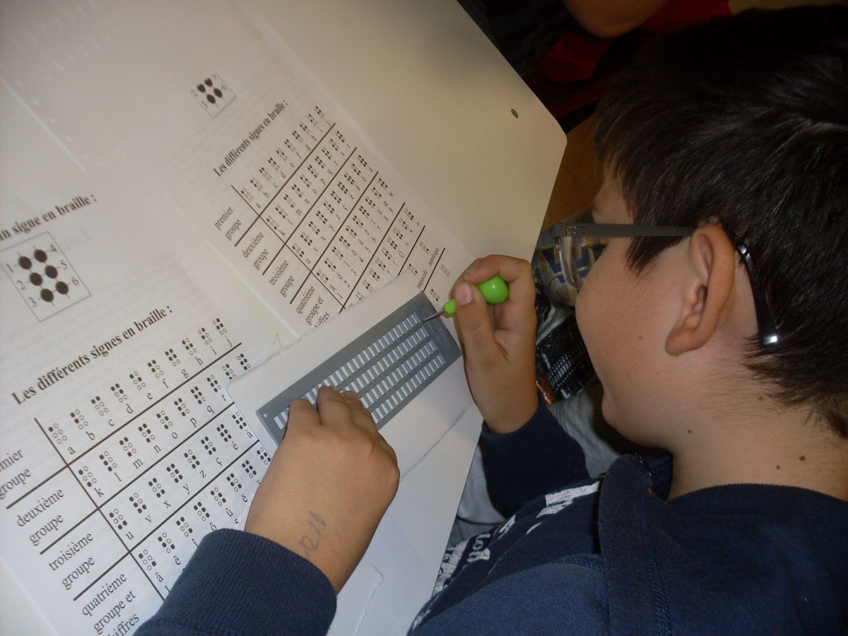 un élève écrit son prénom en braille, avec la tablette et le poinçon